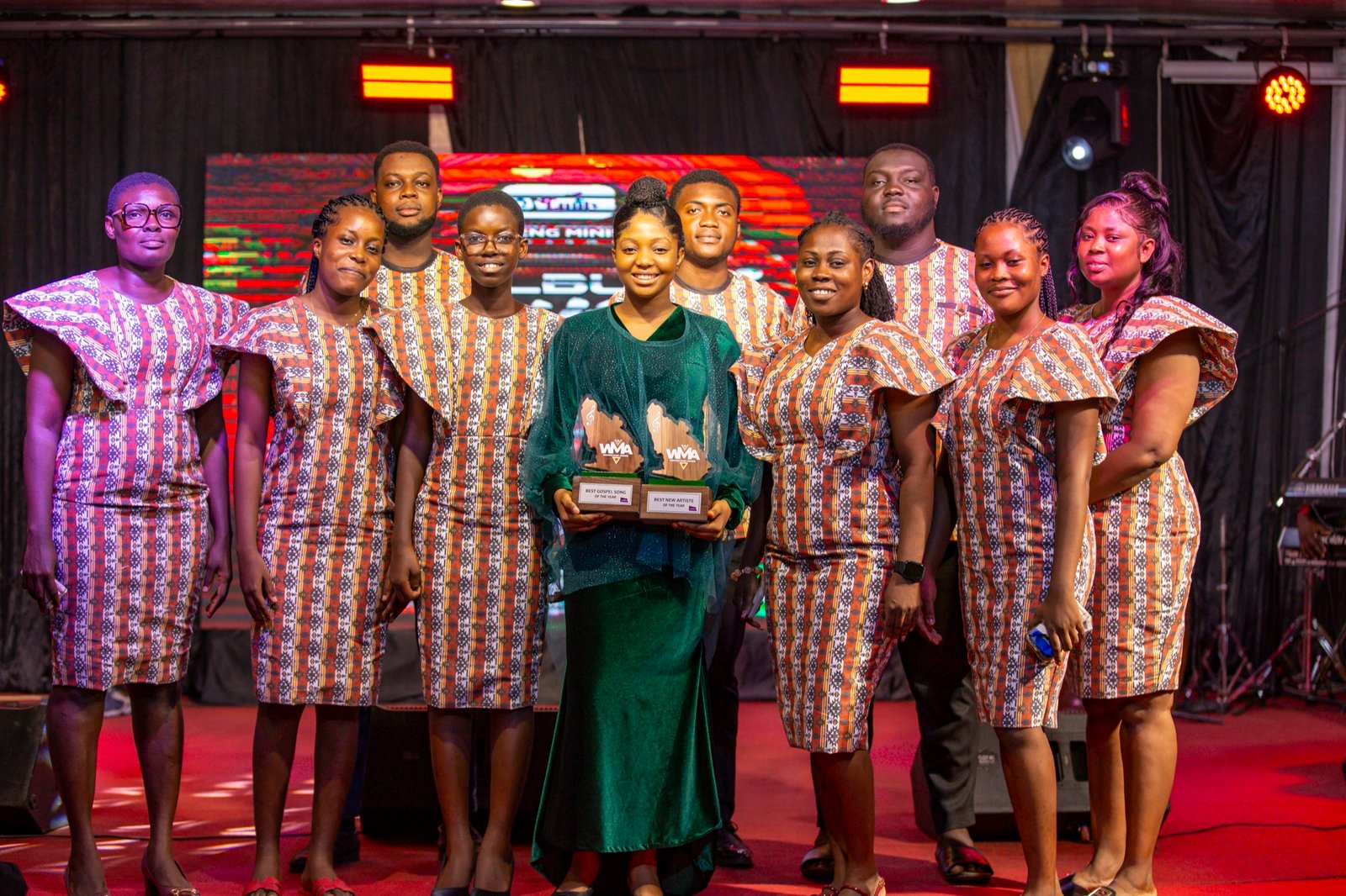 Emily Adade Boateng on stage at the Western Music Awards holding both trophies, surrounded by her ministry team